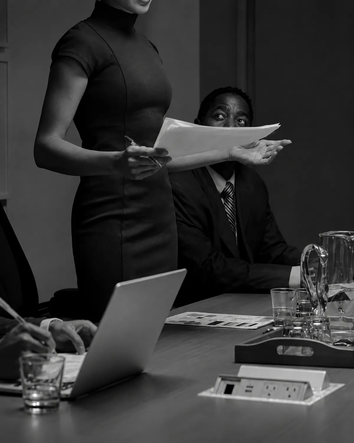 Black-and-white meeting scene with colleagues reviewing documents around a table